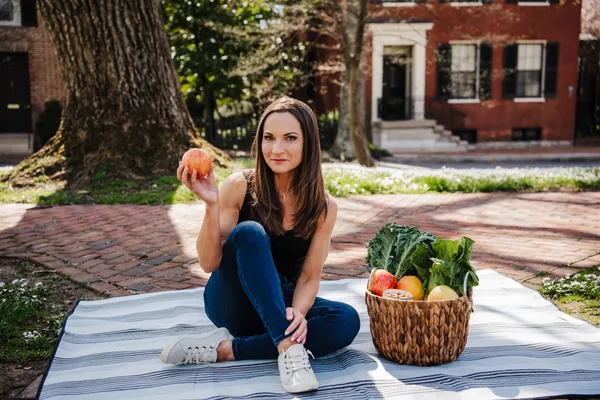 A woman sitting on the ground holding an apple.