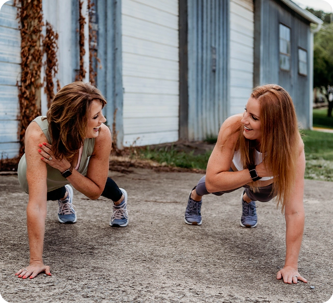 Two women are doing push ups on the ground.