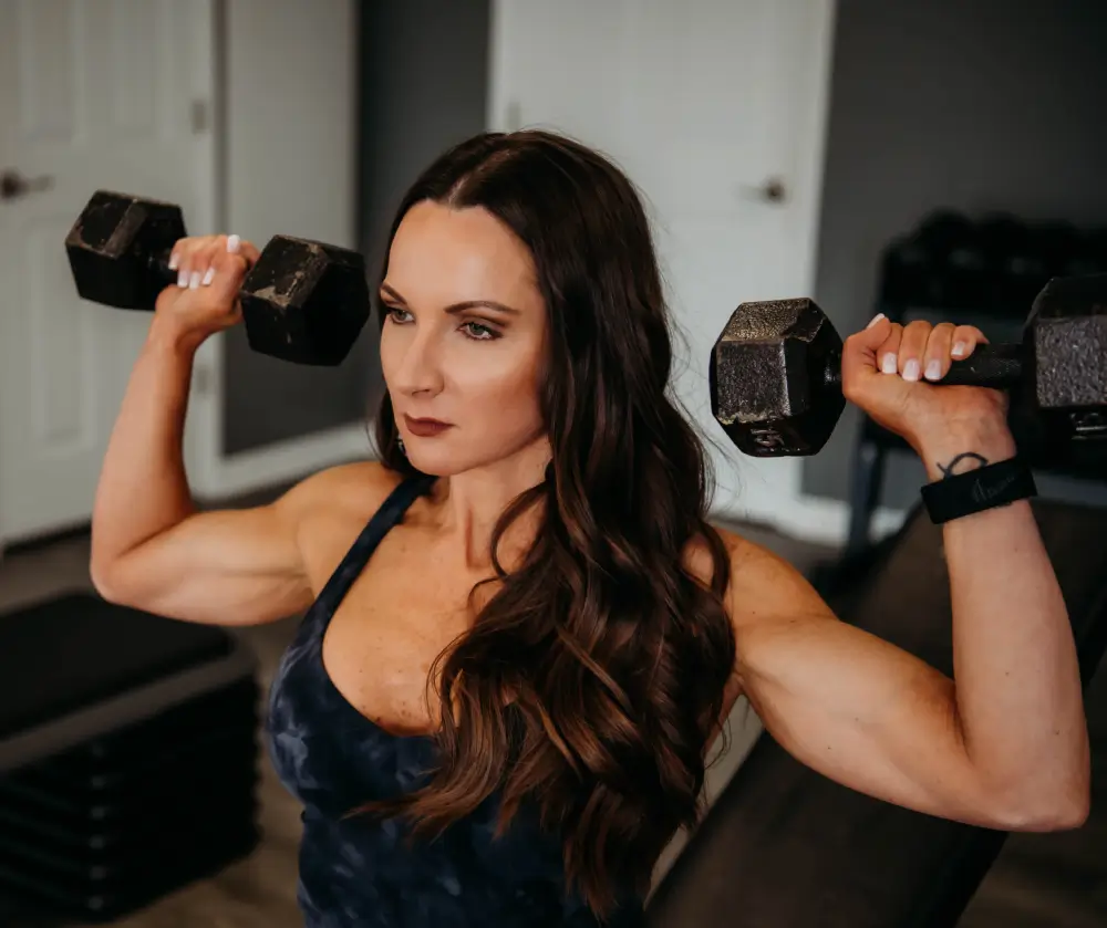 A woman is holding two dumbbells in her arms.